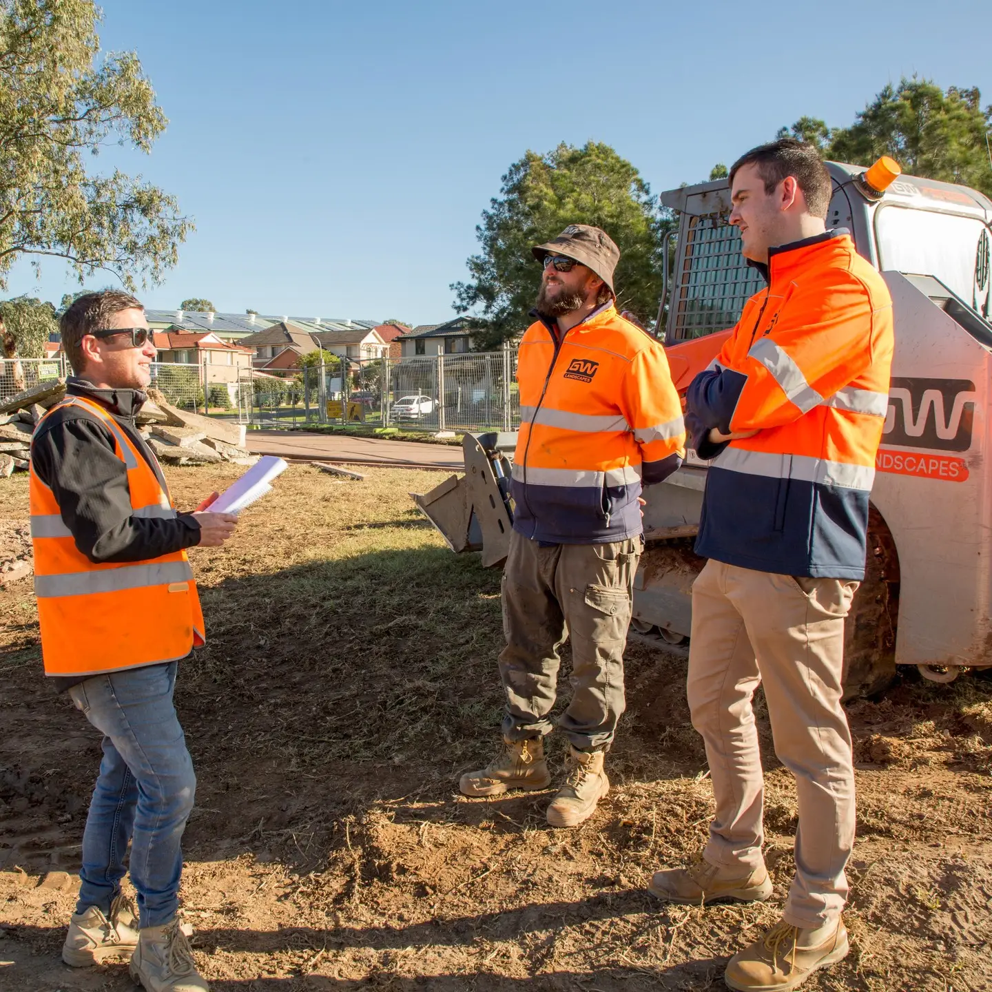 A photo of three skilled Greater West Landscapes construction workers talking during a regular toolbox chat.